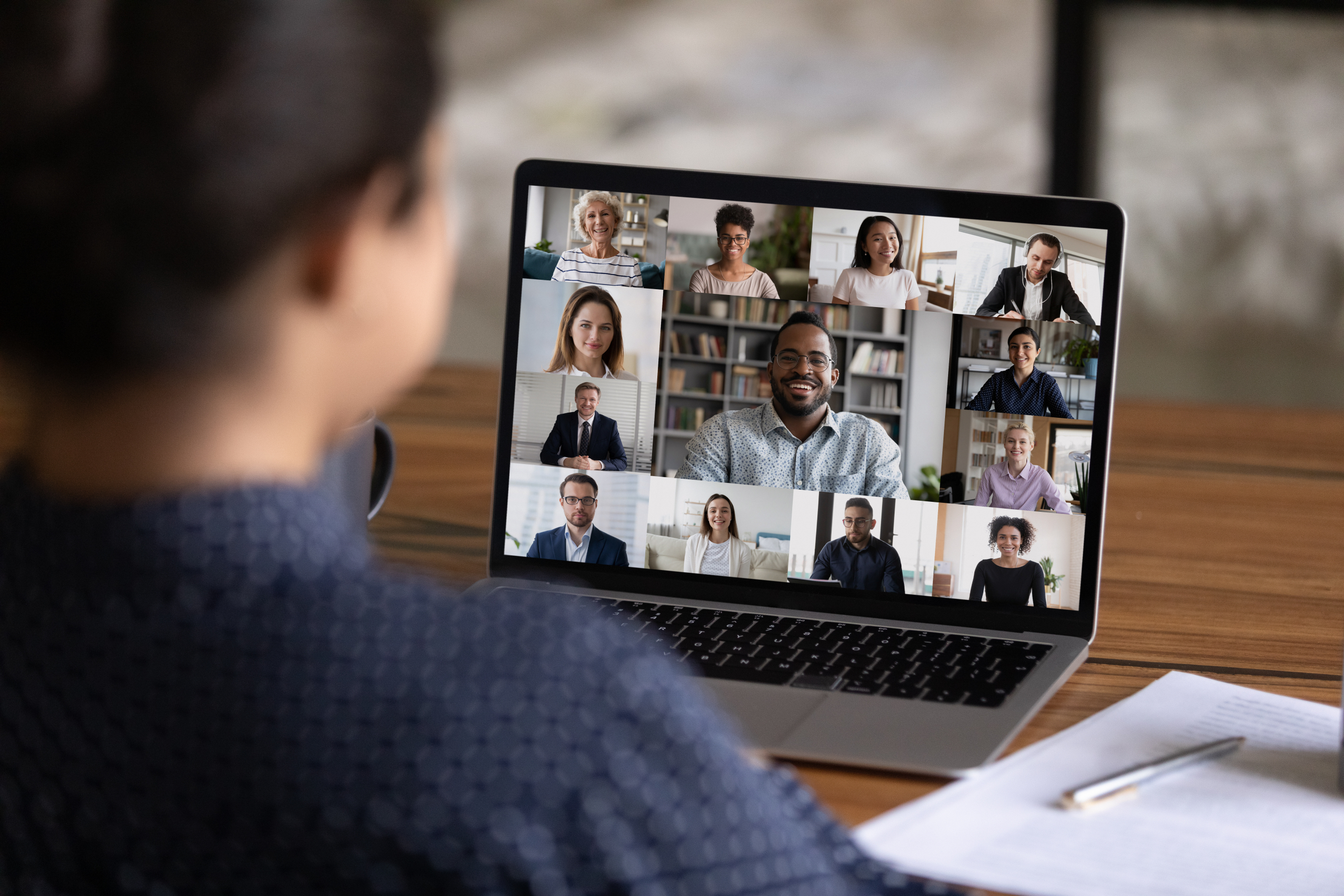 Over shoulder view of female worker have webcam digital virtual conference with diverse multiethnic colleagues. Woman speak talk on video call with businesspeople. of people. Online meeting concept.