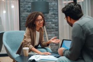 smiling consultant advising client in modern office, relaxed coaching or career advising session with laptop, documents, coffee