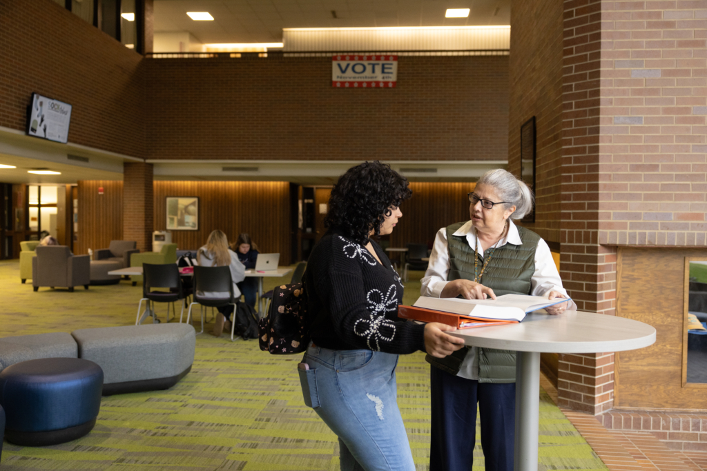 Student listening to an instructor in a common area on a college campus.